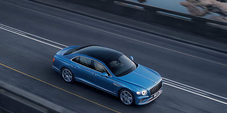 Bentley Melbourne New Bentley Flying Spur Azure sedan in Light windsor blue paint by Mulliner, with 22 inch Azure wheels seen from overhead driving dynamically on a country road