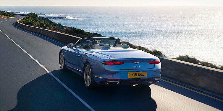 Bentley Melbourne New Bentley Continental GTC Azure convertible rear view in Light Windsor blue paint with 22 inch ten spoke wheels driving dynamically on an ocean road in the sunshine