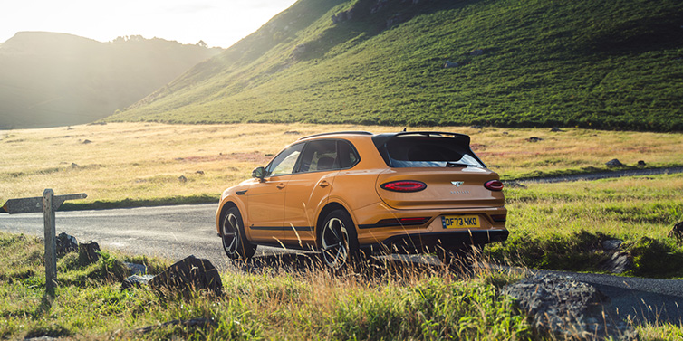 Bentley Melbourne Bentley Bentayga S SUV rear three quarter in Sunburst Gold paint on a road surrounded by green hills