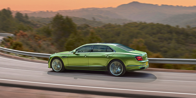 Bentley Melbourne Bentley Flying Spur Speed sedan side profile in Tourmaline Green paint driving dynamically on a mountain road at sunset