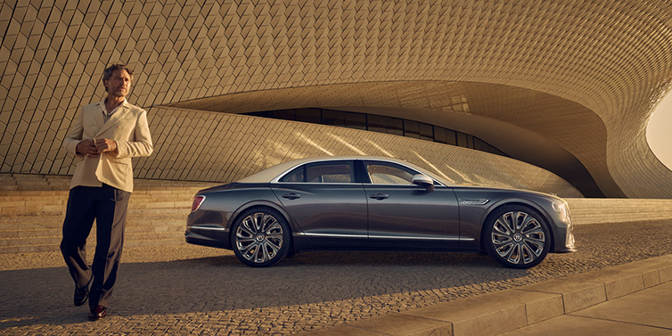 Bentley Melbourne Bentley Flying Spur Mulliner sedan in Rose Gold over Magnetic duotone paint parked by a curved wall with person in suit jacket standing on the left